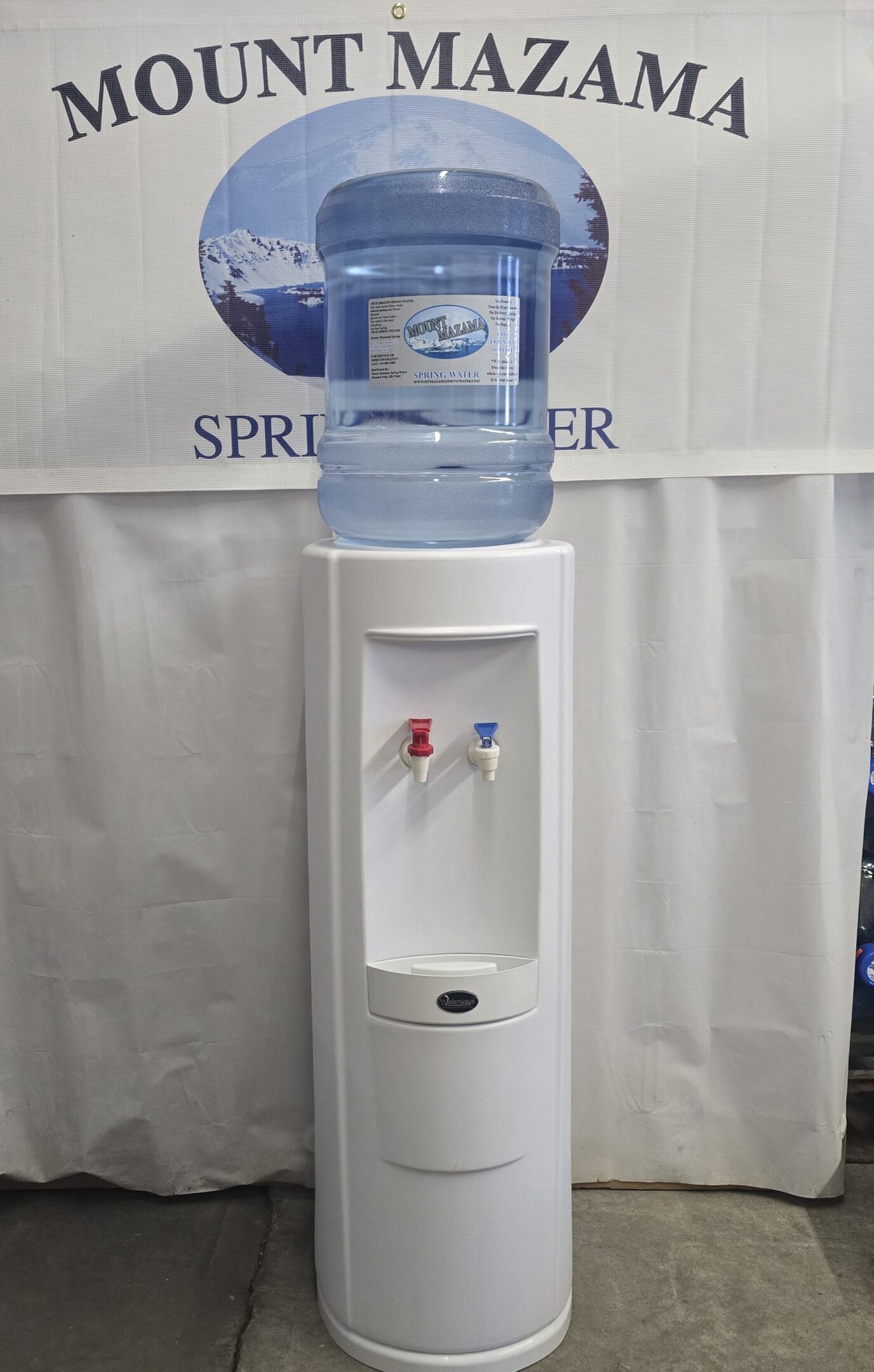 A white water dispenser with hot and cold taps and a large water bottle on top.
